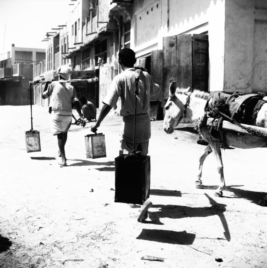 حمالا مياه حافيَي القدمين يحملان المياه في أوعية معاد تدويرها في الخبر.
